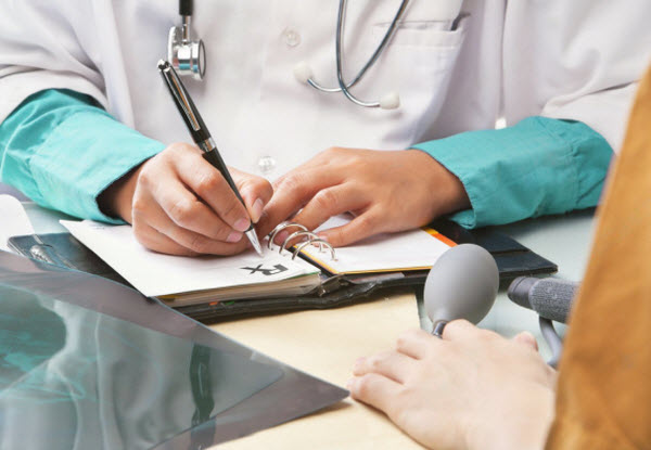 Doctor writing a prescription in front of patient, focus on the hand