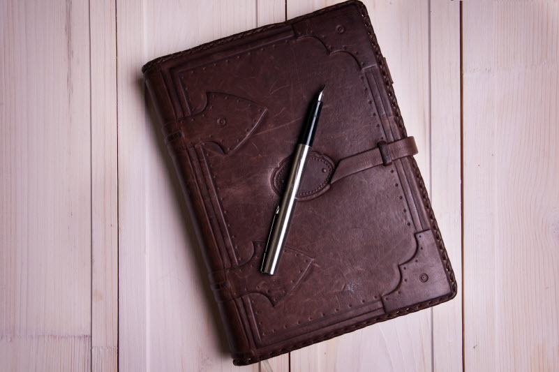 old leather notebook and fountain pen on old wooden boards